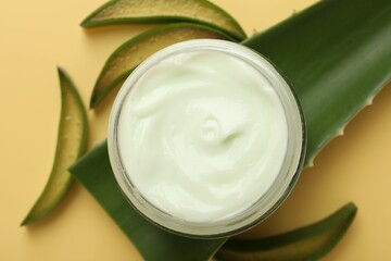 Wall Mural - moisturizing cream with extract of aloe vera in jar and cut leaves on yellow background, flat lay