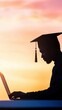 © Exnoi - Graduate Silhouette at Sunset Working on Laptop with Cap and Gown