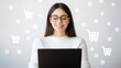 © Chanagun - A joyful woman with glasses smiles while working on her laptop, surrounded by shopping icons, symbolizing e-commerce success.