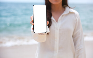 Wall Mural - mockup image of a woman holding and showing mobile phone with blank desktop screen by the sea