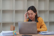 © Phimwilai - Young asian businesswoman suffering from headache while working on laptop computer at office desk, feeling tired, exhausted, having migraine symptoms, massaging temples, relieving pain