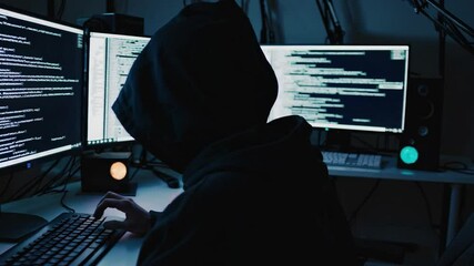 Hacker in dark room typing code on multiple monitors with cybersecurity themes. 4k stock footage