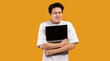 © Prostock-studio - Technology Lover Concept. Happy excited asian man hugging laptop with black blank empty screen, holding it tight near chest. Geek posing isolated over orange studio background wall, copy space