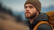 © Nataliia_Trushchenko - Man with a beard and a brown hat is standing in a field. He is wearing a backpack and a jacket