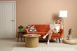© Pixel-Shot - Young woman using laptop and sitting on cozy sofa in beige living room
