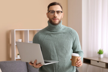 Young freelancer with laptop and cup of coffee in living room
