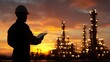 © tuiphotoengineer - A worker s silhouette stands in the foreground against the backdrop of an illuminated oil refinery complex during a vibrant  colorful sunset sky