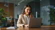 © GS-Studio - Businesswoman at Desk: A focused businesswoman, sits at her desk in a modern office, working on a laptop and looking happy and successful.