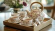 © arthit - A beautifully arranged tea set with a floral teapot, matching cups, and saucers, placed on a wooden tray with tea bags.