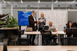 © Drobot Dean - Diverse business colleagues, including a White senior man and an adult Caucasian woman, review documents and presentations around a wooden table during a corporate team meeting in a modern office.