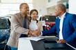 © Anastasiya - A young African American couple happily shakes hands with a dealership manager while finalizing their car purchase agreement at a car showroom, surrounded by vehicles.