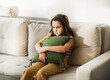 © zulfiska - Child sitting alone on sofa feeling stressed unhappy, sad and depress. Little girl embracing pillow.