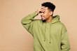 © ViDi Studio - Young sad man of African American ethnicity wear green hoodie casual clothes put hand on face facepalm epic fail mistaken omg gesture isolated on plain pastel light beige background Lifestyle concept