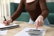 © New Africa - Budget. Woman with paperwork and calculator at wooden desk indoors, closeup