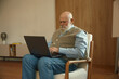 © Nomad_Soul - Retired senior man using laptop computer sitting on comfortable armchair at home