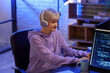 © Pixel-Shot - Female programmer with headphones working in office at night