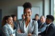© Pete - Young black businesswoman portrait. Confident leader stands with arms crossed in front of diverse team. Professional executive exudes success, ambition, determination in corporate environment.