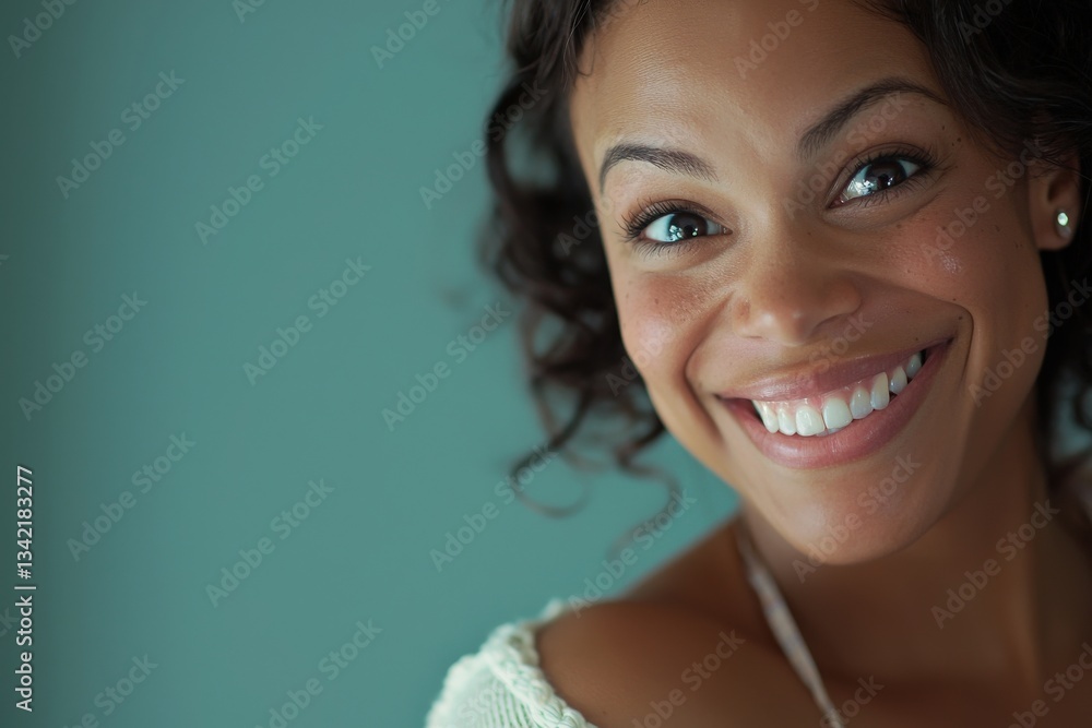 A woman with curly hair and bright eyes smiles warmly at the camera. She exudes joy and confidence in a serene and inviting atmosphere, capturing a moment of happiness.