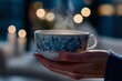 © Undersea - Steaming floral teacup held in feminine hands against blurred bokeh lights background, creating cozy atmospheric mood with rising vapor and blue pattern details.