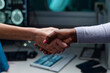 © pressmaster - Two people of different races shaking hands, captured in a medical office with advanced technology and monitoring equipment visible