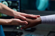 © pressmaster - Close-up of two people holding hands in a medical setting, one wearing a white sleeve and the other a professional uniform showing compassion and support