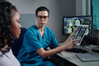 © pressmaster - Nurse showing patient MRI images on tablet while sitting beside computer. Professional medical consultation held in modern healthcare facility with advanced technology present