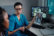 © pressmaster - Medical professional explaining diagnostic imaging results displayed on tablet to patient. Monitor screens in background showing detailed brain scans