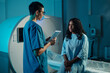 © pressmaster - Two healthcare professionals discussing medical imaging results inside hospital. Medical personnel wearing uniforms while collaborating on patient diagnostics with advanced equipment in background