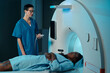 © pressmaster - Medical professional wearing blue scrub assisting patient lying inside MRI scanner in clinical setting without using natural light