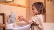 © treephwood - Young girl is carefully lathering her hands with soap while standing at the bathroom sink, emphasizing the importance of hygiene