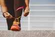 © Prostock-studio - Start of day and workout. African american girl with fitness tracker in trendy sportswear tying shoelaces on bright sneakers at stadium, cropped, close up, copy space