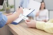 © New Africa - Patient with medical insurance card and receptionist filling document at wooden counter in clinic, closeup