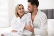 © New Africa - Spa. Happy couple in bathrobes sitting on bed indoors