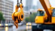 © sakon - A closeup of a yellow crane hook with raindrops, set against an urban background with buildings and vehicles.