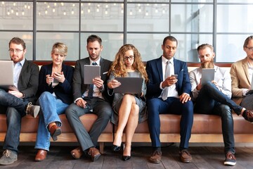Wall Mural - group of diverse professionals sitting on a bench, using laptops and phones. business women and men,