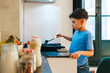 © Alberto - Latin boy using a spatula while cooking something in a frying pan in a modern kitchen