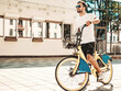 © halayalex - Portrait of handsome smiling stylish hipster lambersexual model.Man dressed in white T-shirt. Fashion male riding a bike on the street background in sunglasses