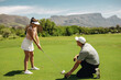 © Jacob Lund - Male golf instructor crouching on green guiding female golfer
