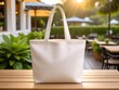 © Tianci - A white tote bag sits on a wooden table, with a blurred outdoor patio and greenery in the background.