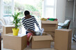 © wavebreak3 - Unpacking boxes, African American woman organizing new home with potted plant nearby, copy space