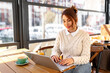 © we.bond.creations - Young woman working on laptop in cafe, enjoying breakfast and urban view