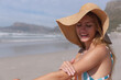 © Wavebreak Media - Smiling woman in sun hat enjoying morning beach sun, applying sunscreen, copy space