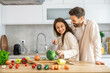 © Dejan - A couple is happily chopping broccoli together, surrounded by colorful vegetables in their cozy and modern kitchen setting.