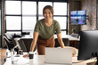 © Wavebreak Media - Smiling woman leaning on desk with laptop and coffee in modern office
