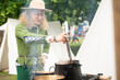 © Soloviova Liudmyla - Smiling young Man in medieval attire straw hat and green tunic, cooks over open flame at historical reenactment event. Reconstructions provide valuable insights into daily life, past eras traditions.