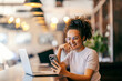 © Dusan Petkovic - Happy girl sitting in restaurant and having video call on cellphone. There is a laptop on a table.