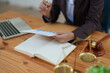 © Jirapong - female attorney advisor at a law firm reviews legal documents at her desk equipped with a laptop notebook and scales of justice in the office