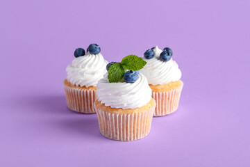 Wall Mural - tasty cupcakes with blueberries on lilac background