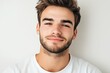 © Veronika - Young man with a confident smile and tousled hair poses against a plain background in a casual white t-shirt