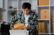 © Natee Meepian - Entrepreneurship and Online Sales. A young man packaging products for e-commerce with a smile.